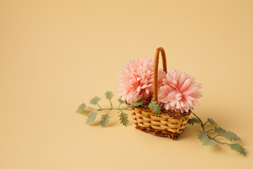 Minimal concept of a small bouqet of pink flowers and leaves in the wicker basket. Vintage spring concept. Beige pastel background. Retro fashion aesthetic.