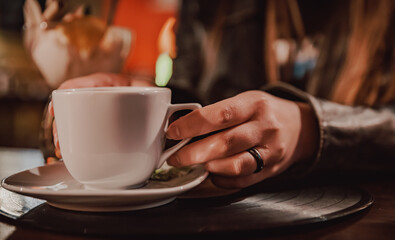 woman hands holding a white cup of tea or coffee standing on the table in cafe