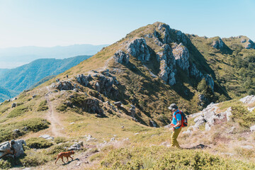 Young man hiking in the mountains with his dog. Beautiful rocky mountain tops in the background