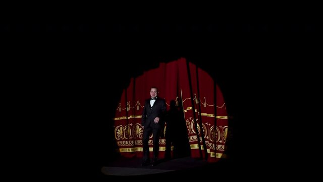 Actor appears on stage. Red curtains open and a theater host in suit comes on the scene on dark background in light spot.