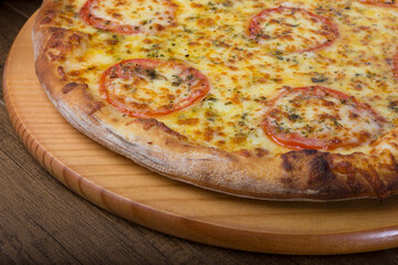 Tasty mozzarella cheese pizza with slices of red tomatoes on a wooden board. Close-up photography. Macro.