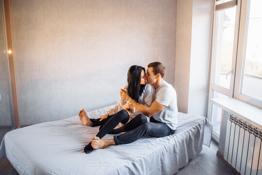 Handsome man with a pumped-up body imperiously hugs his girlfriend. Ready to have sex in a snow-white bed at home. They embrace sensibly during foreplay. Hold each other's hands