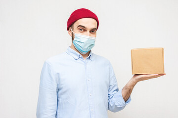 Courier in a medical mask shows paper box. Portrait, white background, copy space, concept of safe delivery goods