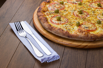 Tasty photograph of mozzarella cheese pizza with sliced ​​red tomatoes. Fork and knife on a napkin.