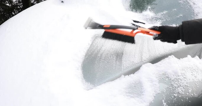 woman cleaning car from snow, Removing snow from car with a brush , Clearing automobile's windscreen from snow