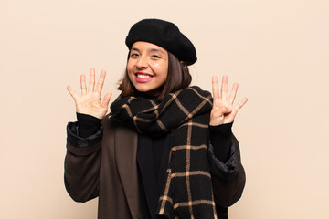 hispanic woman smiling and looking friendly, showing number nine or ninth with hand forward,...
