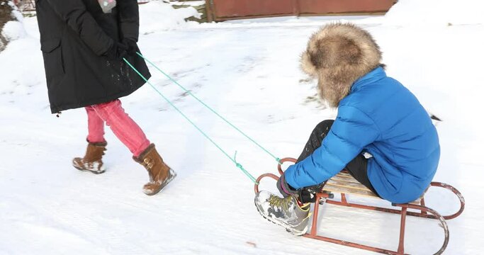 mom pulls son sitting in the sledge, mother pulling little son on sledge