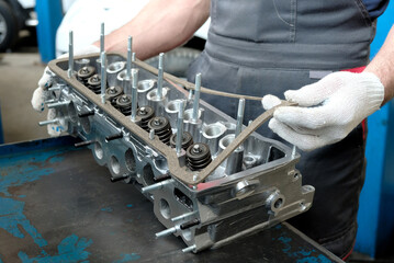 Car parts close-up on the desktop in the service center. A mechanic inspects the cylinder head...
