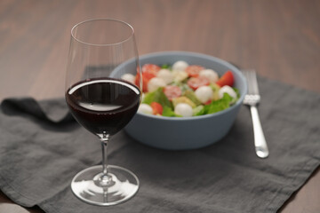 Glass of red wine with salad with romaine, tomatoes and mozzarella in blue bowl