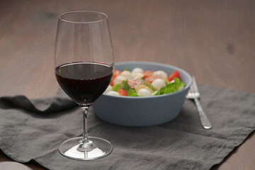 Glass of red wine with salad with romaine, tomatoes and mozzarella in blue bowl