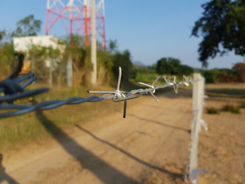 Close-up, Barbed Wire Fence, Walkway And Wave Tower, Mobile Phone Signal Blurred In Background, Clear Sky