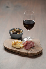 olives, salami and vintage cheese with glass of red wine on walnut table