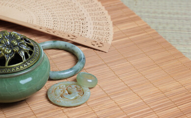 Chinese incense burner, traditional nephrite jewelry and on the bamboo mat background. still-life. copy space.