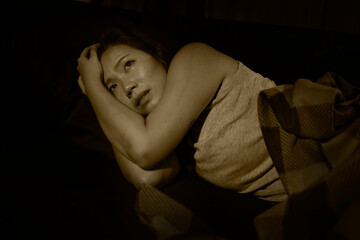 Asian woman suffering depression - dramatic artistic portrait of young beautiful sad and depressed Chinese girl in pain helpless on couch at home in the dark