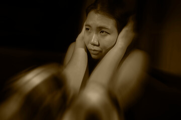 Asian woman suffering depression - dramatic artistic portrait of young beautiful sad and depressed Korean girl in pain helpless on couch at home in the dark