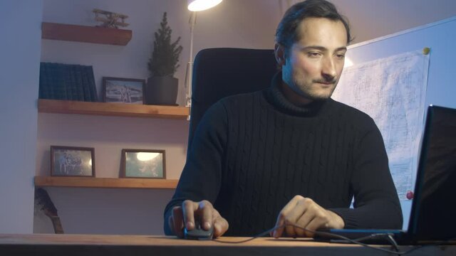 Work at home In the evening with artificial lighting. A man working on a project behind a laptop against the background of a home interior