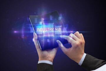 Obraz premium Businessman holding a foldable smartphone with INDUSTRY 4.0 inscription, new technology concept