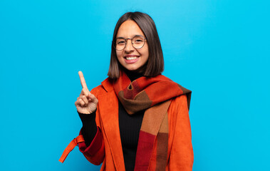 hispanic woman smiling cheerfully and happily, pointing upwards with one hand to copy space