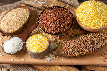 White and red rice, buckwheat, amaranth seeds, corn groats, quinoa and millet in bowls on a brown wooden table. Gluten-free cereals. Top view