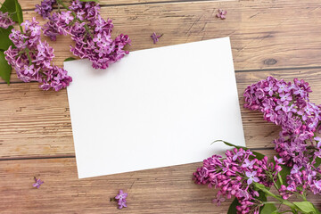 Obraz na płótnie Canvas White blank sheet of paper with blooming lilac flowers on wooden background. Invitation or greeting card for Valentine's Day and Mother's Day. Top view, flat lay, mock up, copy space. Spring concept.