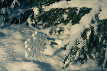 Big shiny festive snowflake hanging on the branch of a fir tree covered with snow in winter. Christmas greeting card. 