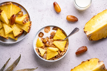 Healthy breakfast bowl: dates with fresh pineapple, homemade granola, corn flakes on light grey background. Flat lay selective focus.