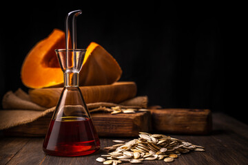 Fresh organic pumpkin seed`s oil in the glass bottle on rustic wooden background close up selective...