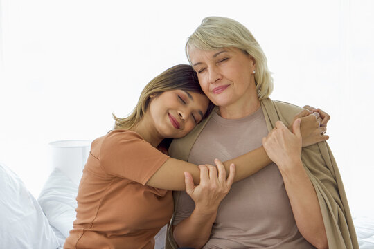 Happy mix skin family living together, asian daughter and adopted caucasian mother cuddle each other with smiles. Concept of love and sharing time of family, mother or daughter in law.