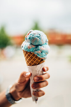 Vertical shot of a cone ice cream with bubble flavor in a girl's hand on abstract background