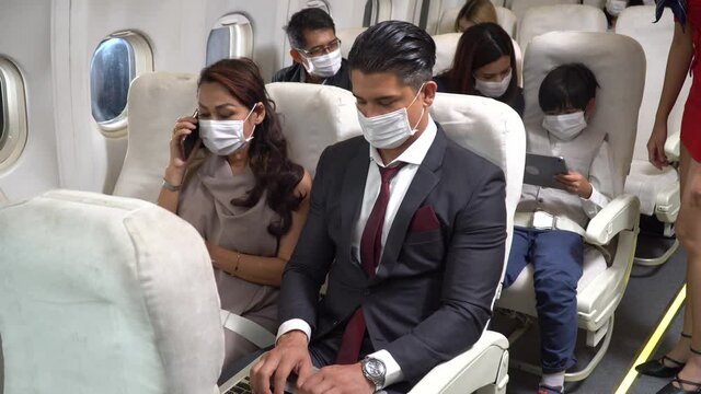 couple business passengers wearing protective mask talking together sitting in airplane. traveling by plane during the coronavirus pandemic or Covid-19 outbreak. woman using phone,  man with laptop