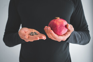 Man hands holding dietary iron or ferrum supplements and fresh pomegranates food for people with...