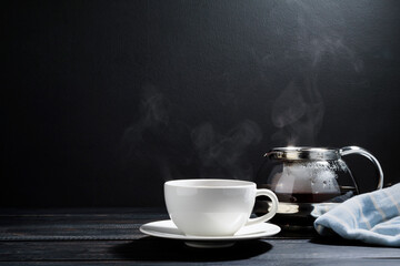 A hot teacup with herbs was placed on an old wooden table in a black background, a gentle sunlight shone in a warm atmosphere.