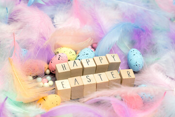 Happy Easter written with wooden cubes surrounded with beautiful pastel colored decorative feathers and eggs, April, Easter, Religion, Spring concept for background and greeting card top view