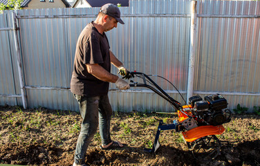 Male in the spring plows the earth in working clothes with a motoblock