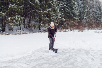 Woman removing snow with a shovel in the winter. Ice rink cleaning