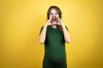 Young beautiful brunette woman pregnant expecting baby over isolated yellow background shouting and screaming loud to side with hands on mouth