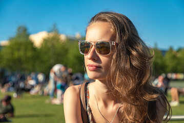 Close up portrait of a beautiful long-haired woman in sunglasses outdoors on a background of public park view.