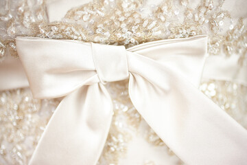 White fabric bow on the background of the lace fabric of the bride's dress. Decoration for the celebration. Focus concept.