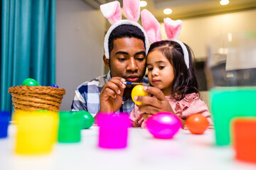 happy mixed race family celebrating Easter, painting eggs with brush smiling and laughing