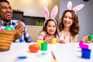 afro american man and caucasian woman ans their cute child painting eggs indoors