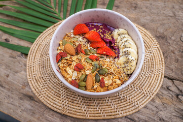 Healthy food Acai breakfast superfoods smoothie bowl with chia seeds, bee pollen, fresh Strawberry, apple, almond, banana and granola for healthy vegan on a wooden table.
