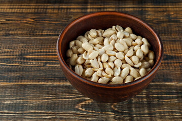 Peanuts in a clay bowl on an old shabby board. Nuts on a brown wooden table.