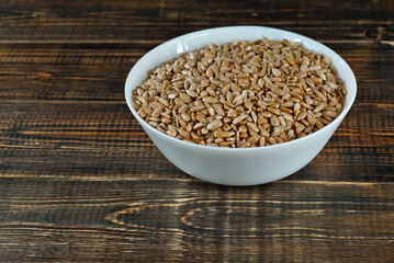 Sunflower seeds in a white bowl on an old shabby board. Nuts on a brown wooden table.