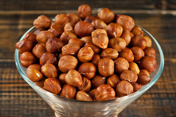 Hazelnuts in a transparent glass bowl on an old shabby board. Nuts on a brown wooden table.