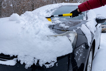 Woman cleans snow from a car after a snowfall.