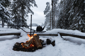 Kettle over an open fire in winter. Burning wood. Winter snowy forest. Lifestyle, camping. 