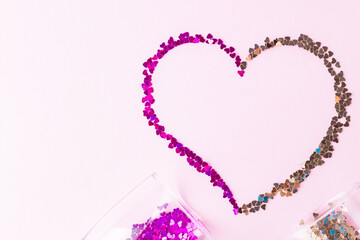 Heart shape made of multicolored glitter. Two champagne glasses with splash of heart shaped confetti over pink background. Valentine's Day concept. Flat lay