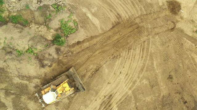 Above top view bulldozer is pushing muddy ground, leveling, equates sediment.