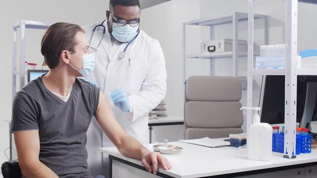 African-American doctor makes a coronavirus vaccine using a syringe and hypodermic needle. Medical worker and patient at the hospital office. Vaccination and safety concept.