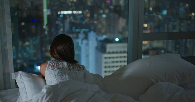 Woman look at the city view and lying on bed at night
